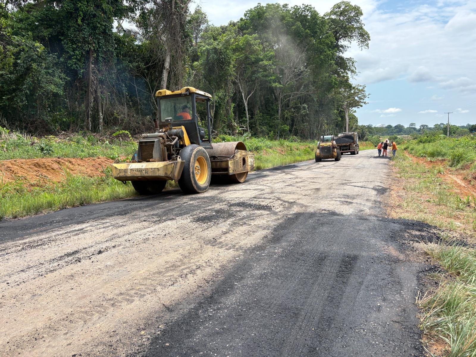 Rolo compactador e caminhão em serviço de tapa-buracos na rodovia RO-257, entre Ariquemes e o distrito de 5º BEC, com trabalhadores ao fundo